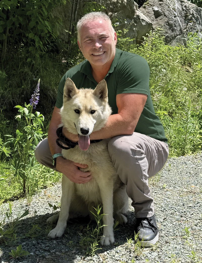 Dr. Mark Roberts holding a dog outdoors with greenery in the background