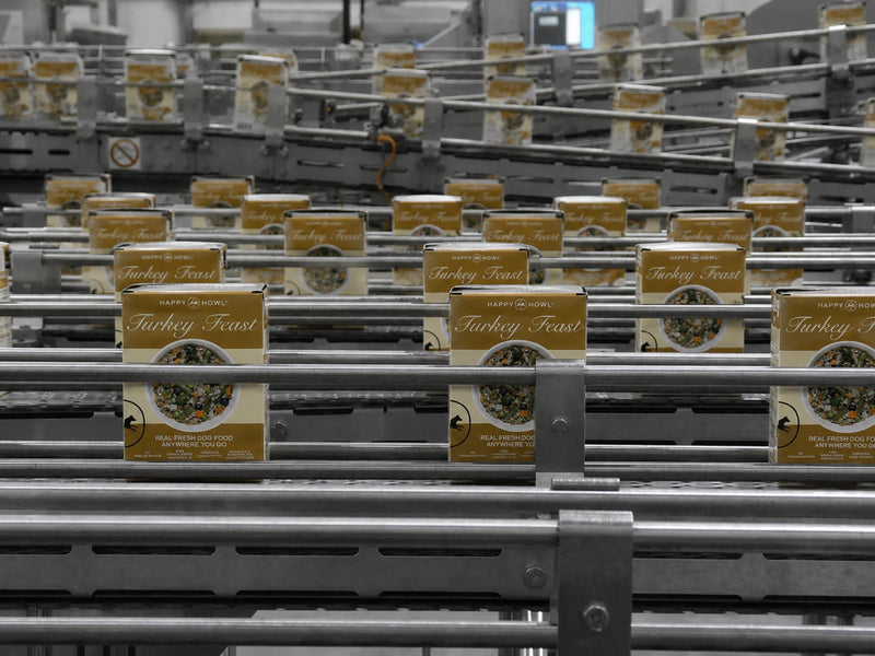 Pallets of 'Turkey Feast' food packages on a conveyor belt in a warehouse.