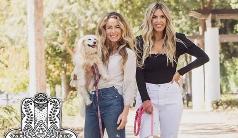 Two women standing outdoors with a dog, one holding a leash.